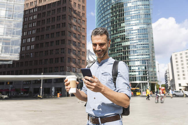 Hombre de negocios sonriente mirando el teléfono inteligente en la ciudad, Berlín, Alemania - foto de stock