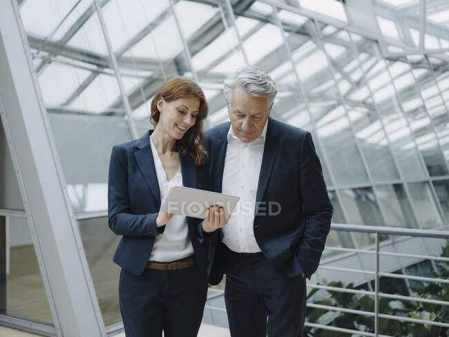Hombre de negocios sonriente y mujer de negocios usando tableta en edificio de oficinas moderno - foto de stock
