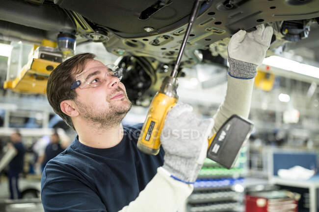 Hombre trabajando en la parte inferior del coche en la fábrica moderna - foto de stock