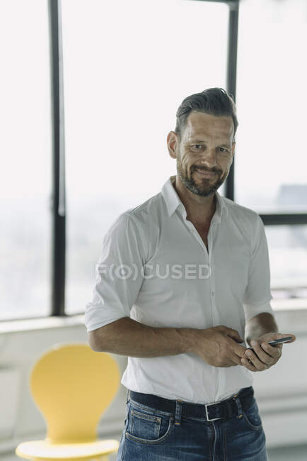 Retrato de empresário maduro confiante com telefone celular no escritório vazio — Fotografia de Stock