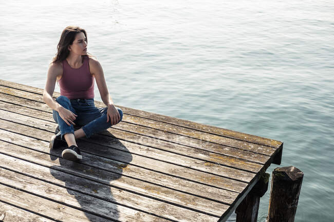 Young woman sitting on jetty looking at distance, Lake Starnberg, Germany — Stock Photo