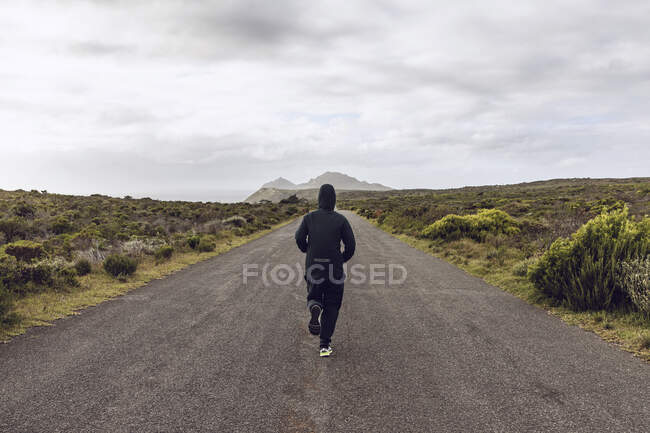 Vue arrière de l'homme faisant du jogging sur route de campagne, Cape Point, Western Cape, Afrique du Sud — Photo de stock