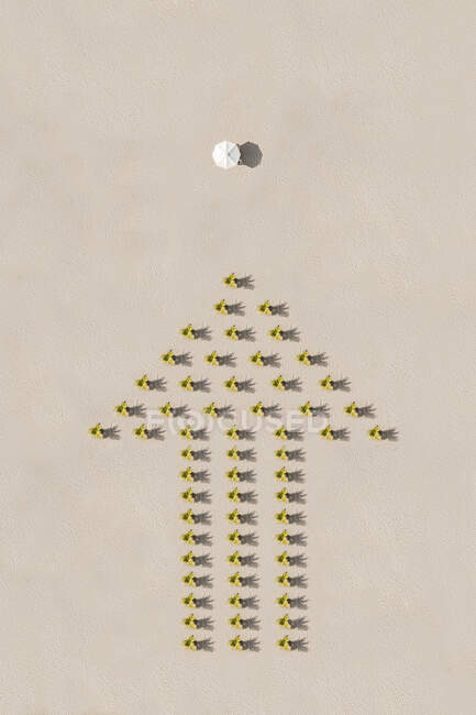 Стрелочный знак желтых цветов на песке, указывающий на пляжный зонтик — стоковое фото
