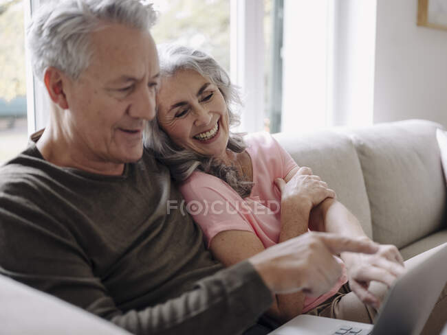 Casal sênior feliz com laptop relaxante no sofá em casa — Fotografia de Stock