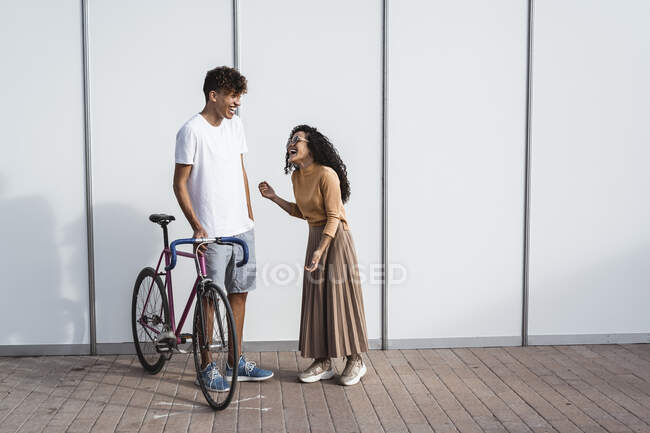 Couple heureux avec vélo debout devant une clôture blanche, riant — Photo de stock