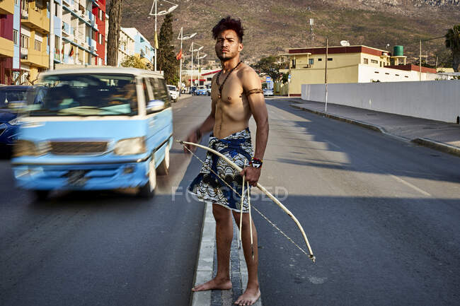 Uomo tribale con il suo arco tradizionale e frecce nel centro della città con auto di passaggio, Lubango, Angola — Foto stock
