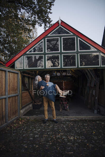 Senior man carrying his wife in front of boathouse — Stock Photo
