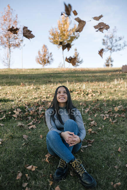 Portrait of happy teenage girl sitting on a meadow watching tumbling autumn leaves — Stock Photo