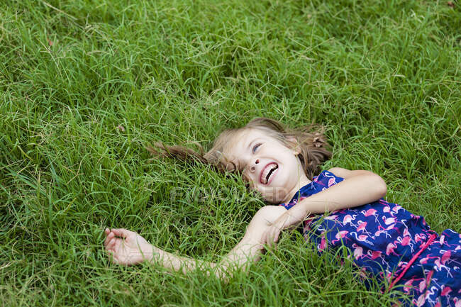 Смеющаяся маленькая девочка, лежащая на лугу летом — стоковое фото