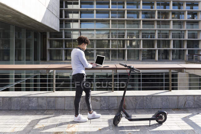 Молодой человек с электронным скутером использует ноутбук в городе — стоковое фото