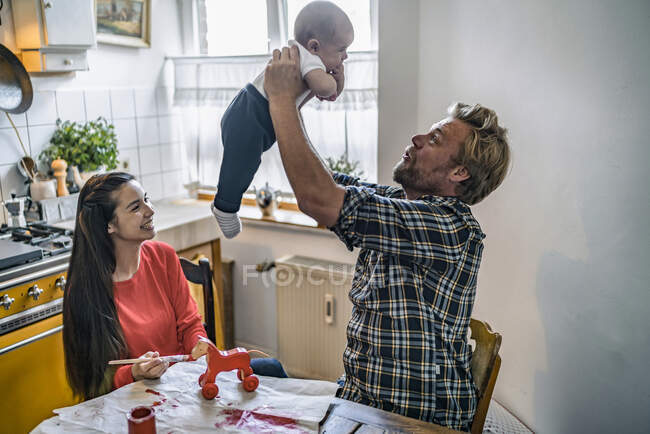 Famiglia che solleva il bambino al tavolo della cucina a casa — Foto stock