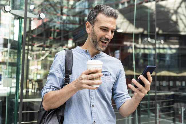 Homme d'affaires heureux regardant le smartphone dans la ville, Berlin, Allemagne — Photo de stock