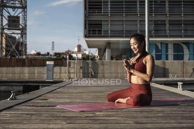 Asian woman practicing yoga, meditating on a pier at habour — Stock Photo