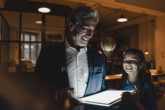 Happy senior buisinessman and girl with hot-air balloon and shining tablet in office — Stock Photo