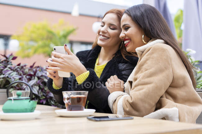 Two female friends using smartphone outdoors at a coffee shop — Stock Photo