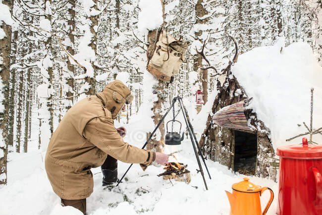 Hombre preparando té en el bosque de invierno junto a un refugio de madera, Estado de Salzburgo, Austria - foto de stock