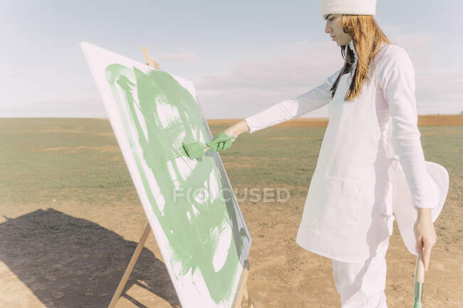 Jeune femme sur champ sec, toile à peindre avec peinture verte — Photo de stock