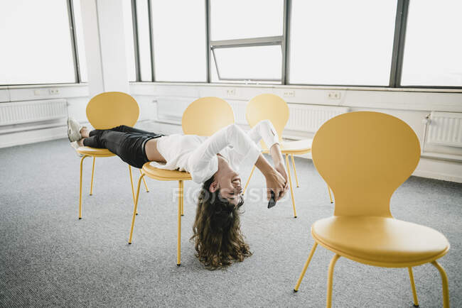 Smiling businesswoman lying across chairs in an empty office using smartphone — Stock Photo