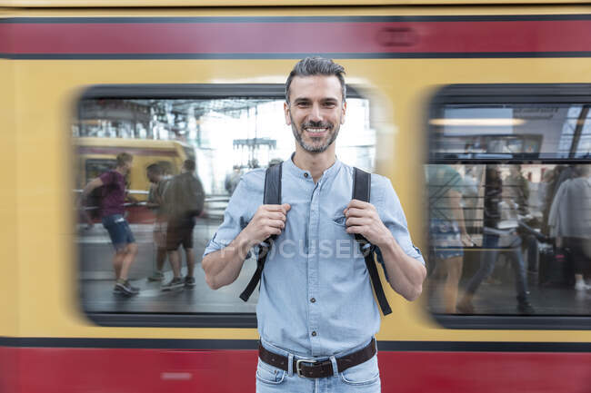 Retrato del hombre sonriente en la plataforma de la estación con el tren en el fondo - foto de stock
