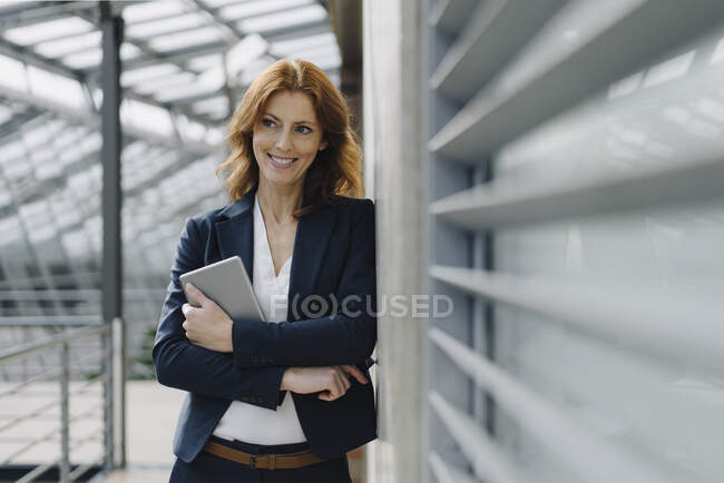 Portrait d'une femme d'affaires souriante tenant une tablette dans un immeuble de bureaux moderne — Photo de stock