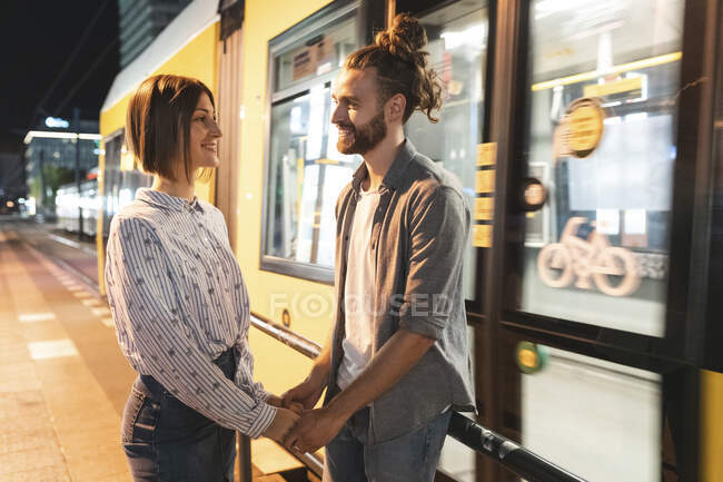 Smiling couple holding hands and looking each other with a tram in the background, Berlin, Germany — Stock Photo