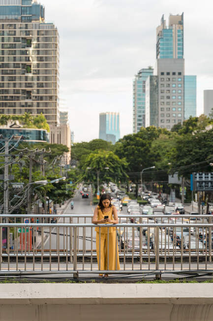 Мовчазна жінка, одягнена в жовтий, стоїть на мосту і дивиться на мобільний телефон у Бангкоку (Таїланд). — стокове фото