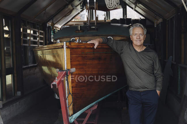 Portrait of a proud senior man at wooden boat in a boathouse — Stock Photo