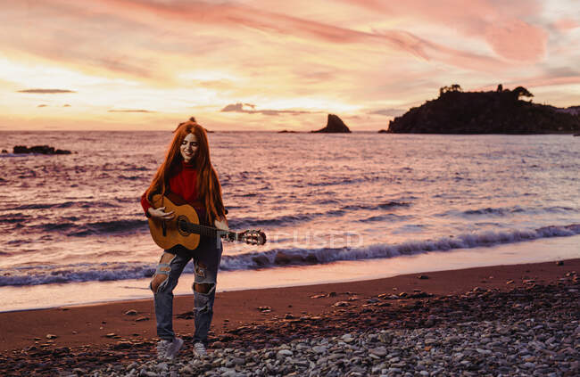 Заруда молода жінка, що грає на гітарі на пляжі на заході сонця (Альмунекар, Іспанія). — стокове фото
