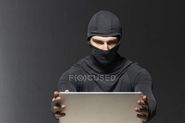 Masked hacker using laptop — Stock Photo