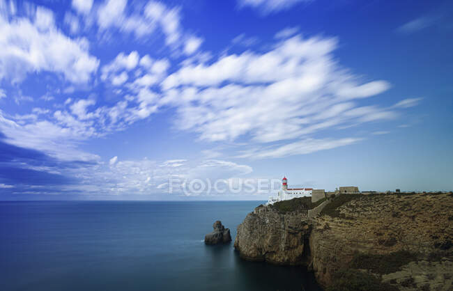 Portugal, Faro District, Lagos, Clouds over lighthouse standing at edge of coastal cliff — Stock Photo