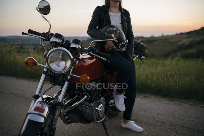 Récolte de jeune femme avec une moto vintage sur la route de campagne au coucher du soleil, Toscane, Italie — Photo de stock