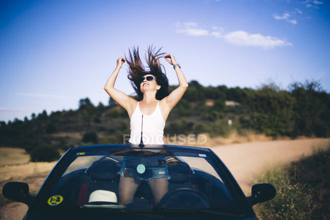 Женщина, стоящая в своем кабриолете, бросающая волосы — стоковое фото