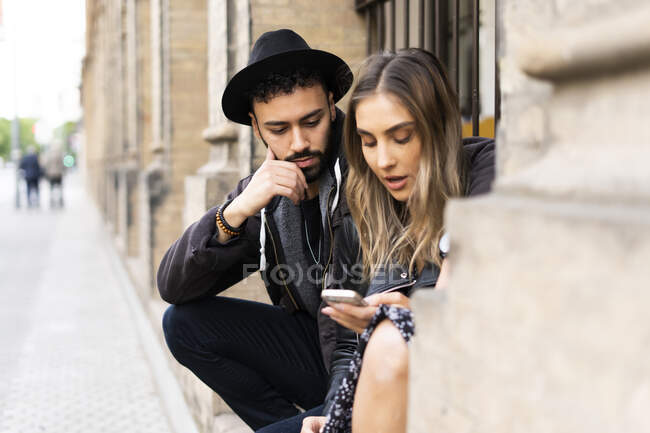 Молодая пара сидит на улице и смотрит на мобильный телефон — стоковое фото