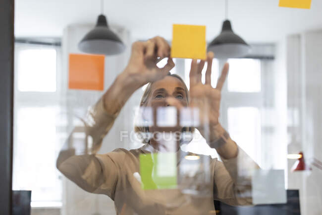 Femme d'affaires mature avec des notes adhésives sur vitre dans le bureau — Photo de stock