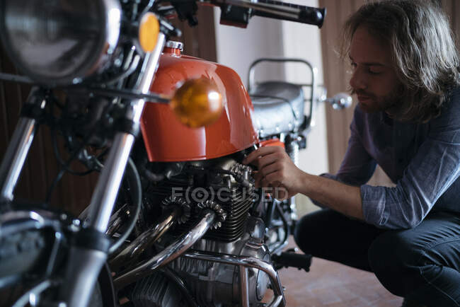 Young man checking his vintage motorbike parked in garage — Stock Photo