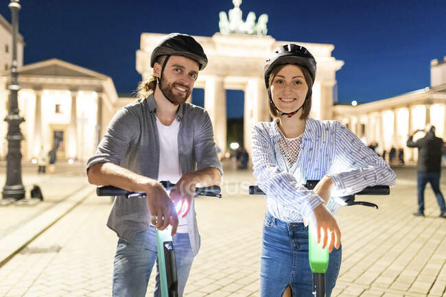 Coppia giovane con scooter elettrici alla Porta di Brandeburgo di notte, Berlino, Germania — Foto stock