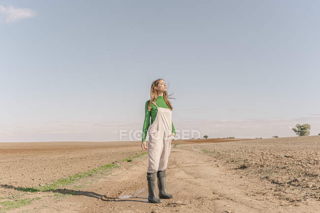 Молода жінка стоїть на сухому полі з закритими очима. — стокове фото
