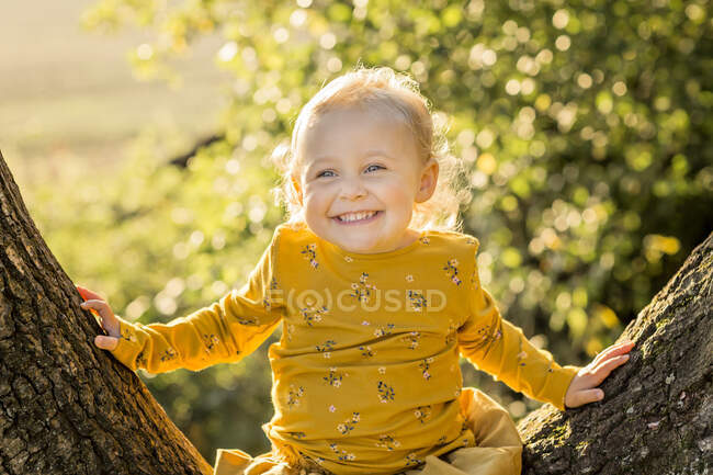 Portrait de jeune fille blonde heureuse assise sur le tronc d'arbre — Photo de stock