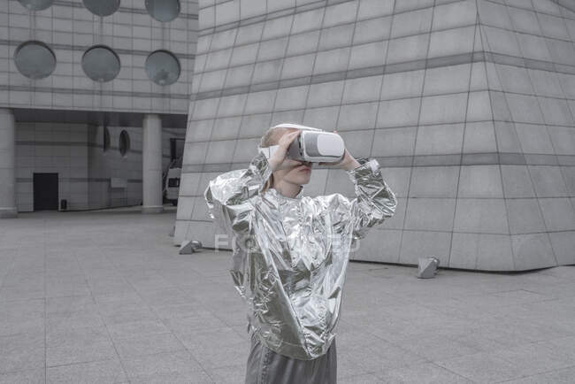 Une fille en costume argenté. regarder à travers les lunettes VR dans la ville futuriste — Photo de stock