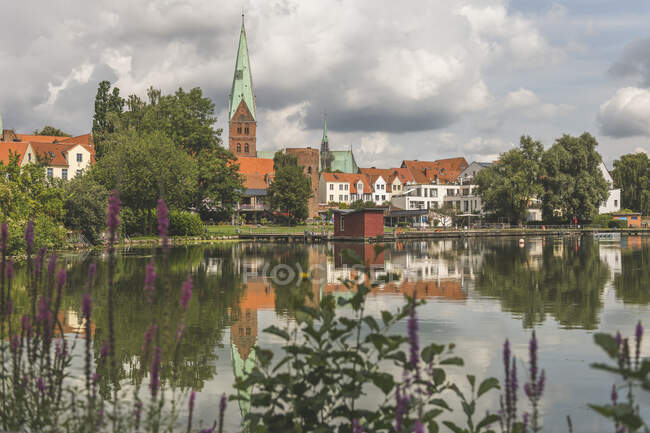 Дома и св. Эгидиен-Кирхе у озера Крхентейх против облачного неба в Леке, Германия — стоковое фото