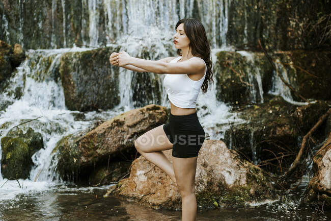 Junge Frau praktiziert Yoga auf einem Wasserfall, Baumstellung — Stockfoto