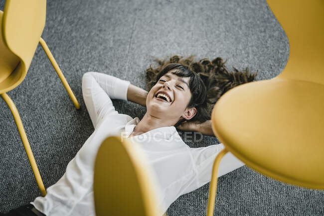 Laughing businesswoman laying in an office on the floor between chairs — Stock Photo