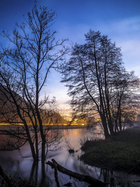 Німеччина, Баварія, силуети дерев проти легких автомобілів, що тягнуться вздовж берега річки Нааб під час заходу сонця. — стокове фото