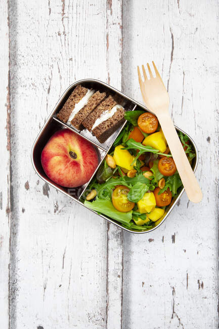 Close-up of lunchbox with mango salad, rye bread sandwich and peach — Stock Photo