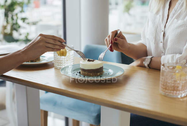 Giovani donne anonime che condividono una torta al coffee shop — Foto stock