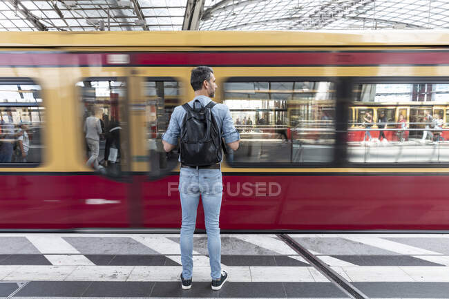 Передній вид людини з рюкзаком на платформі станції під час поїзда, що прибуває — стокове фото