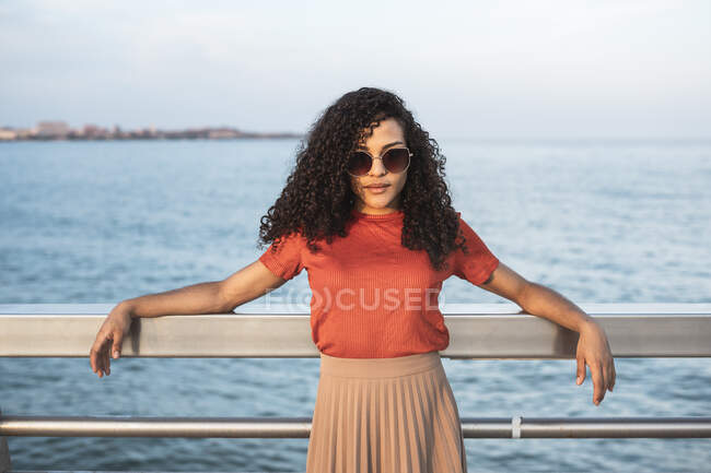 Красива жінка у сонцезахисних окулярах спирається на поручні біля моря. — стокове фото