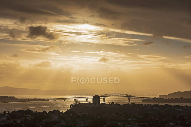Silhouette Auckland Harbour Bridge over sea against sky at sunset, New Zealand — Stock Photo