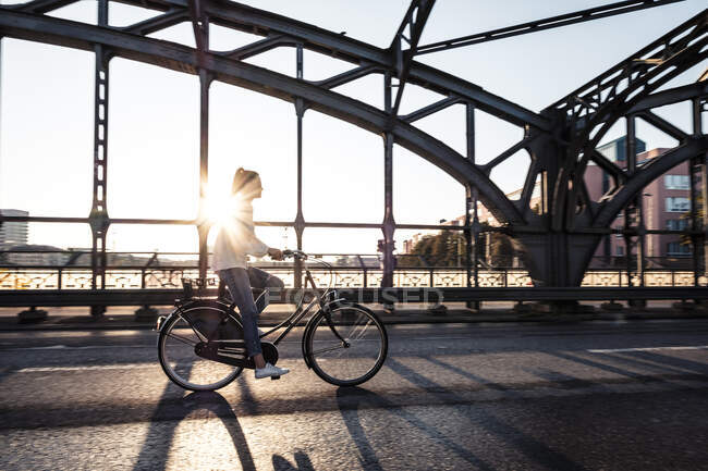 Giovane ciclista su un ponte al tramonto — Foto stock