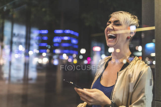 Portrait of laughing blond woman using mobile phone at night, Berlin, Germany — Stock Photo